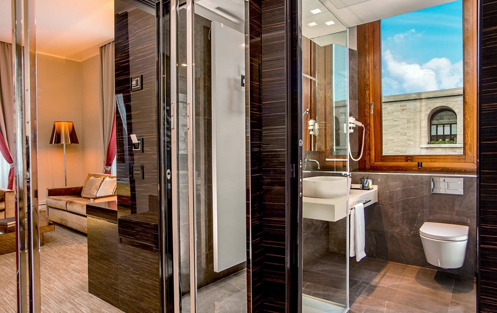 L'hôtel dispose d'une chambre moderne avec de grandes fenêtres offrant une vue enchanteresse. Dotée d'une salle de bains carrelée avec des appareils muraux, une élégante cloison en verre la sépare de l'espace nuit confortable orné d'un canapé et d'un lampadaire, reflétant l'élégance d'un hôtel-boutique.