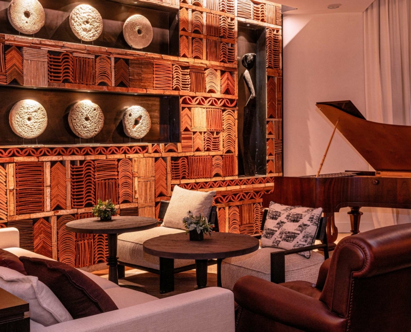 Le salon confortable du Dolce by Wyndham Versailles | Domaine du Montcel comprend des fauteuils modernes, une chaise en cuir, une table basse ronde, un piano à queue et un mur texturé orné de motifs géométriques, d'œuvres d'art sculptées et d'un éclairage doux.